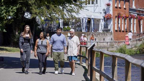 A diverse group of people walking by a river on a sunny day