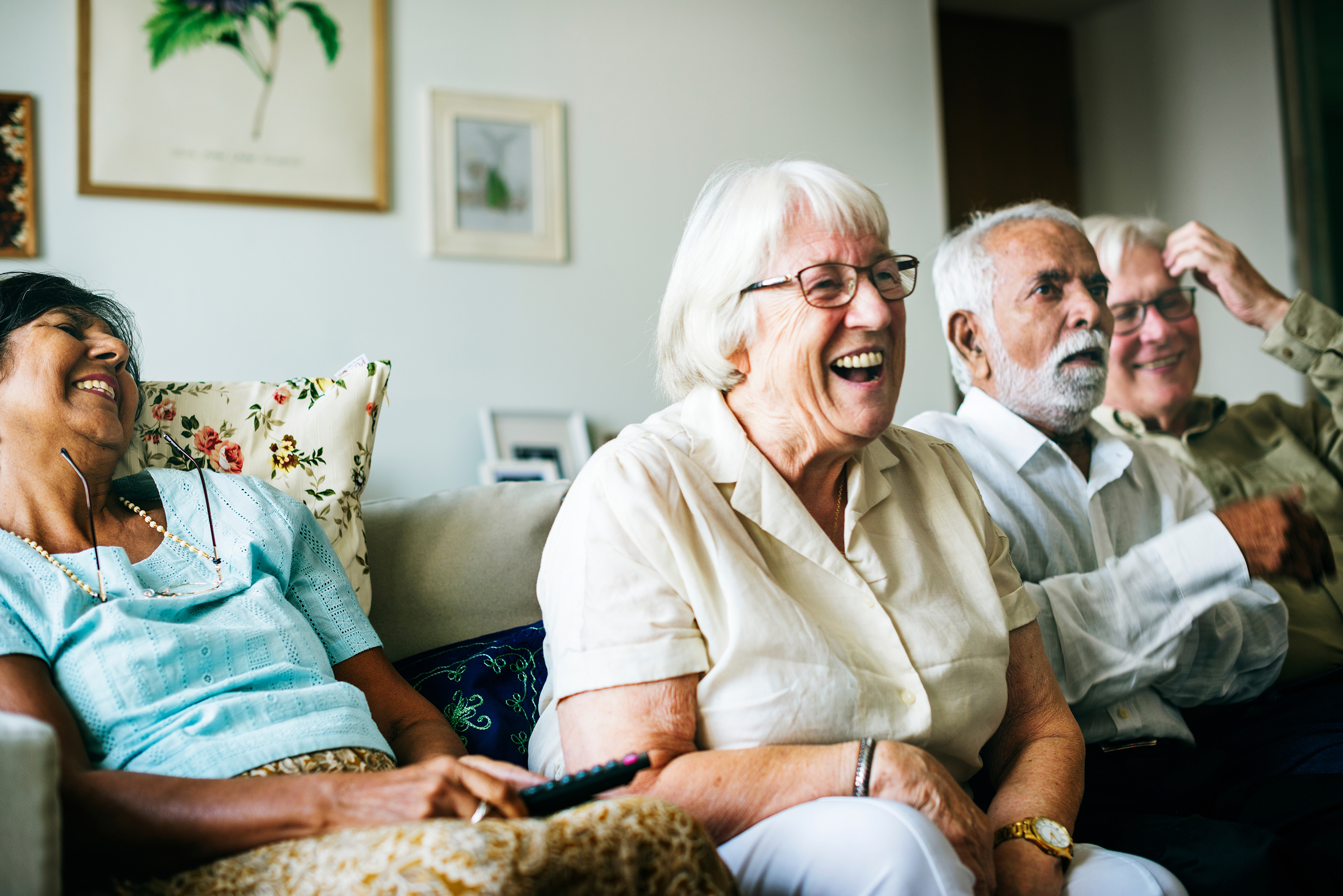 A group of two older women and two older men sitting on a sofa spending time together and laughing 