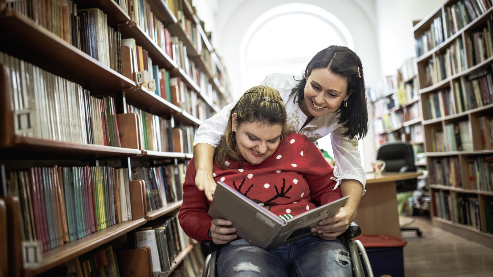 A woman reads to a girl in a wheelchair at the library