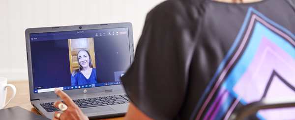 A woman at the office speaks to another woman via a video call on a laptop