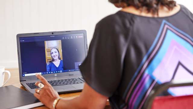 A woman at the office speaks to another woman via a video call on a laptop