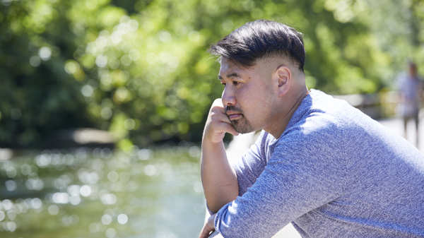 A man stands and looks out the river with a look of contemplation 