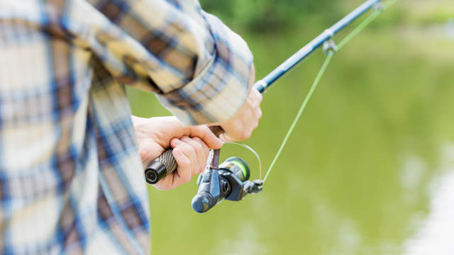 A man holds a fishing pole over a lake.