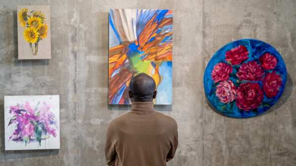 A man looks at paintings at a gallery