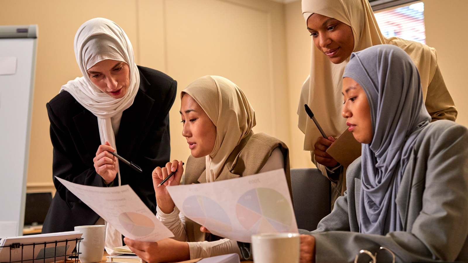 Four Muslim women lock at pie graphs at work