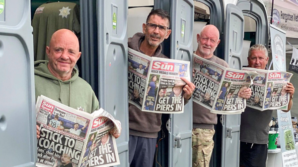 Four men stand at a doorways and hold up the Sun newspaper