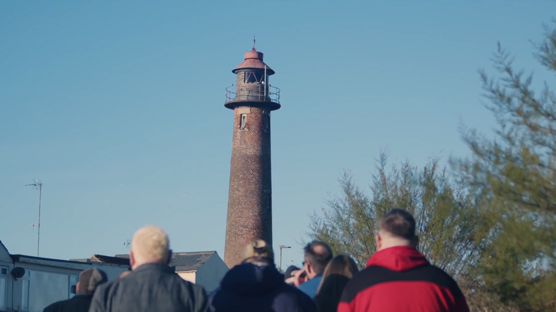 People walking outside, a lighthouse in the background 