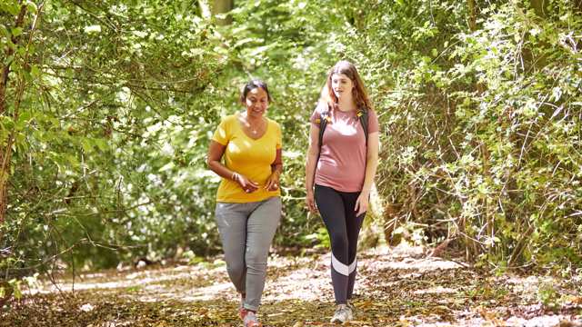 Two women talk as they walk through a wooded path