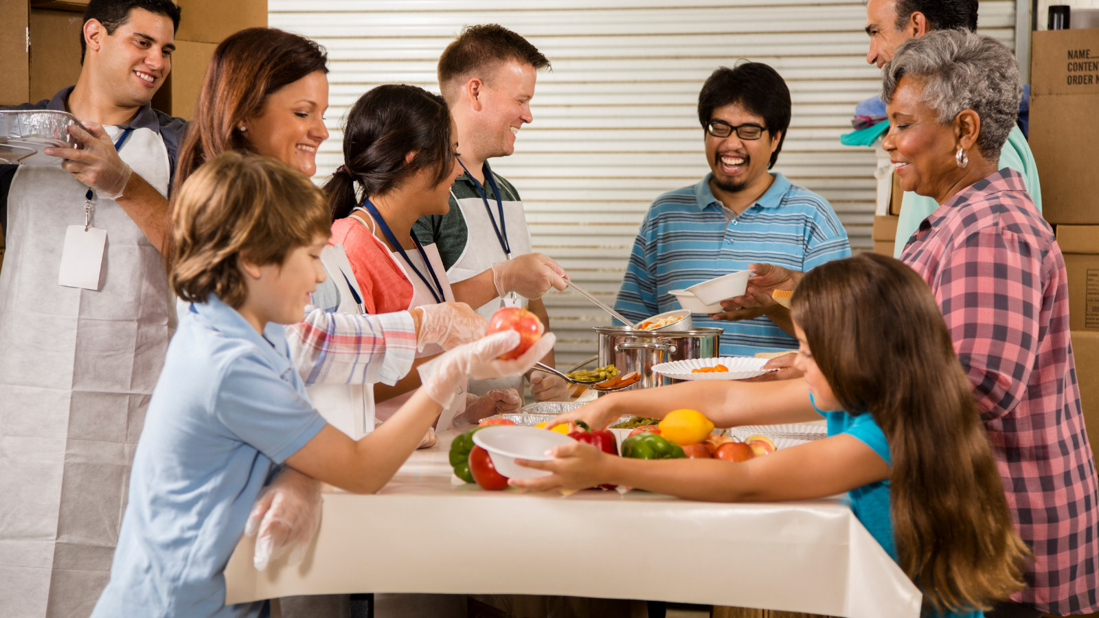 A group of adults and children of different ethnicities cook a meal together