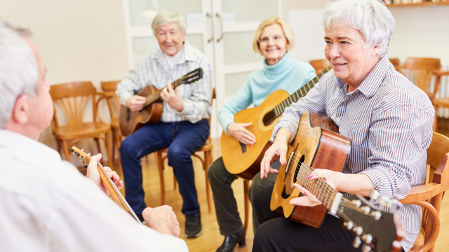 Four older adults sit in a line and line and play classical guitars