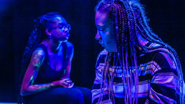 Two black women sit in a dimly lit auditorium