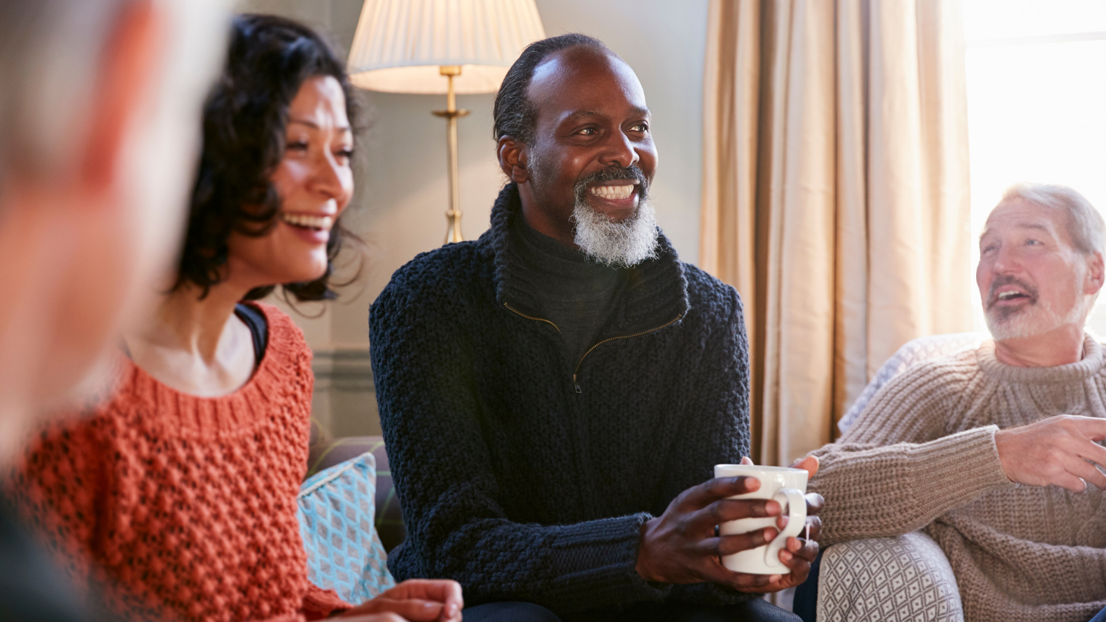 A group of adult laugh and drink tea during a social meeting