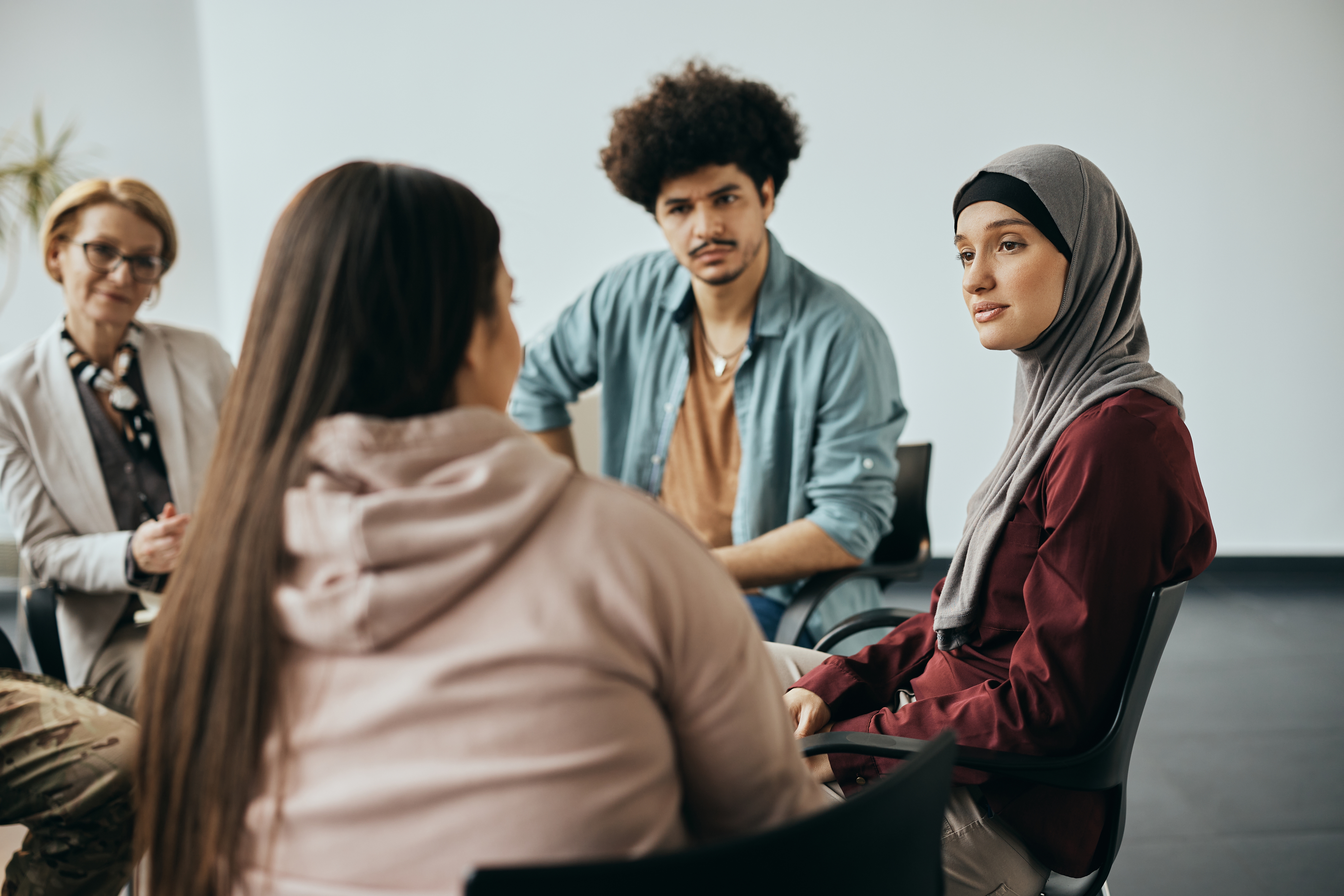 A diverse group of young people sat in a circle with an older woman offering advice and information