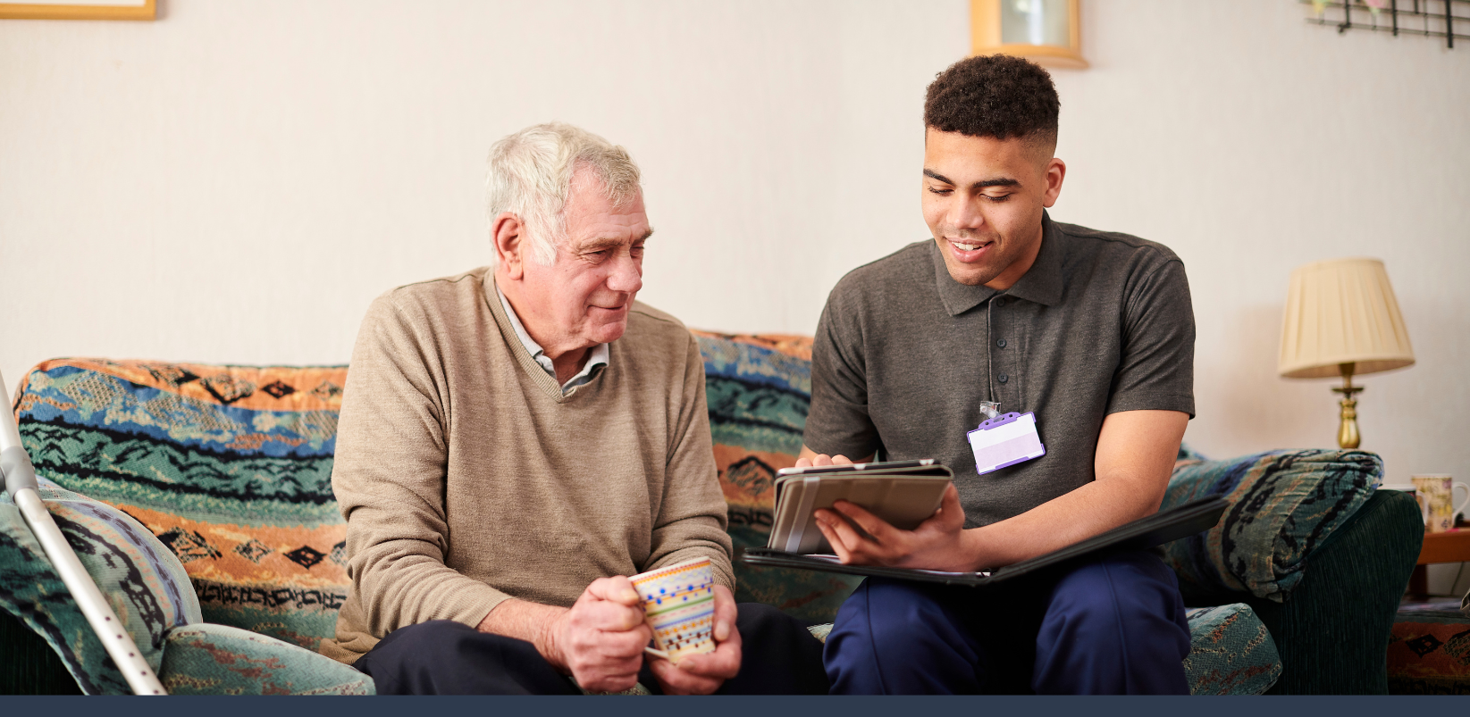 An older man is sat on a sofa with a young link worker and are looking at his notebook together