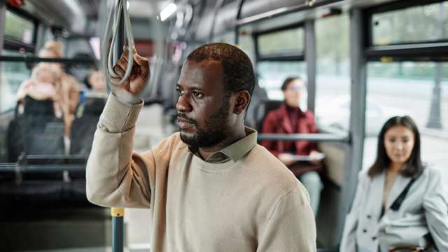 A man stands alone on a bus holding onto the rail and looking out of the window 