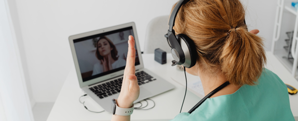 A healthcare professional sitting wearing headphones and speaking with someone over video call