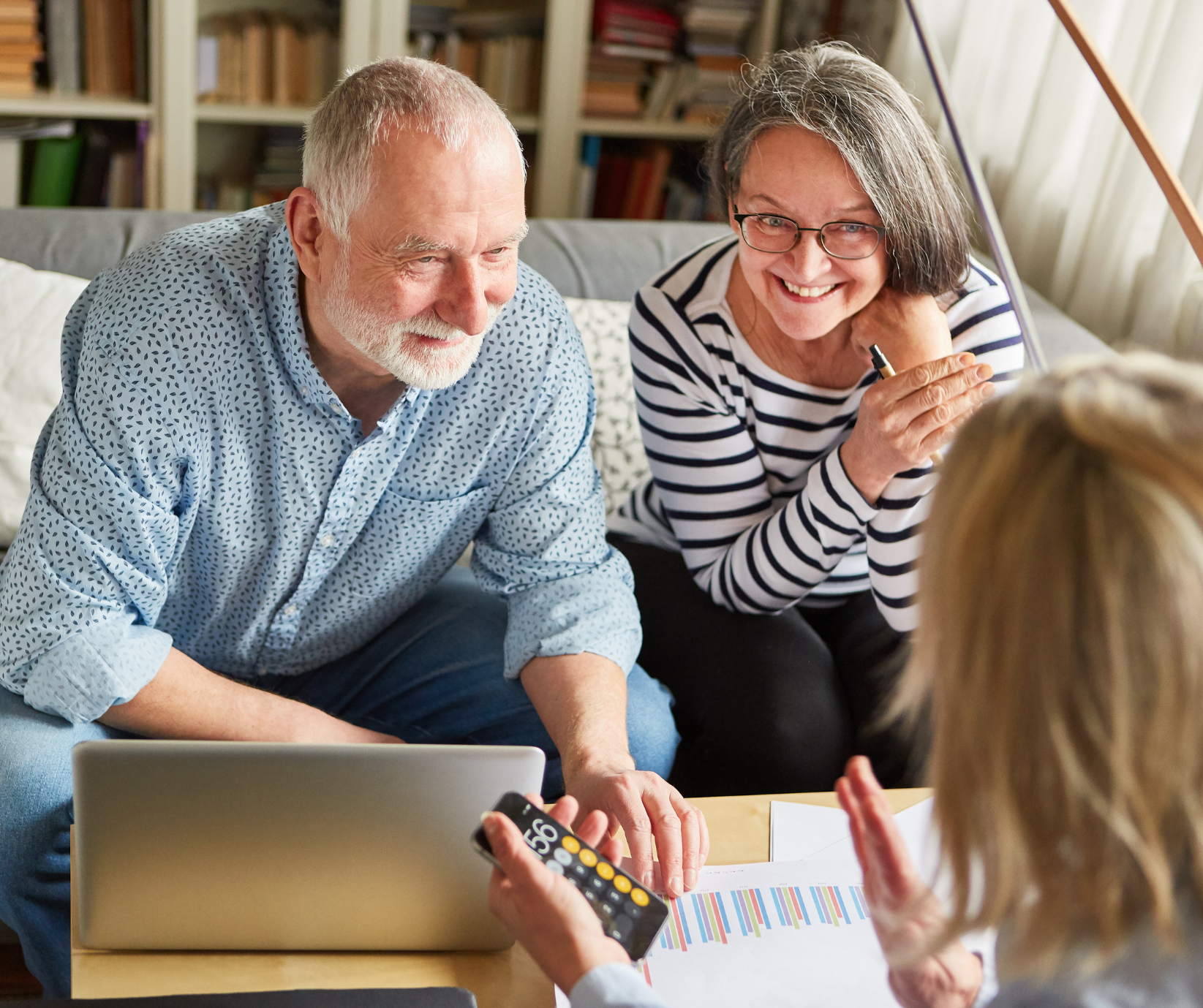 An elderly couple are sat on a sofa with a laptop talking to a woman with a calculator
