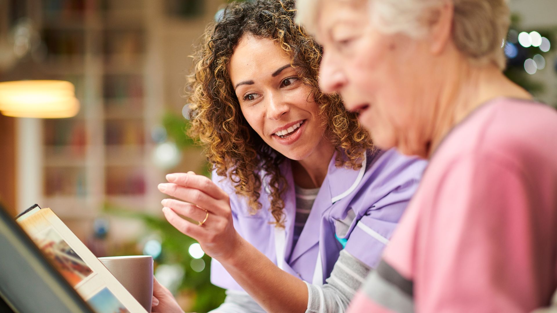 Two ladies are chatting together and smiling, looking at a photo album together
