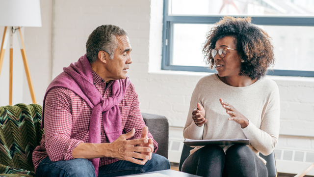 A man sits on a sofa and talks to woman sitting in a chair next to him