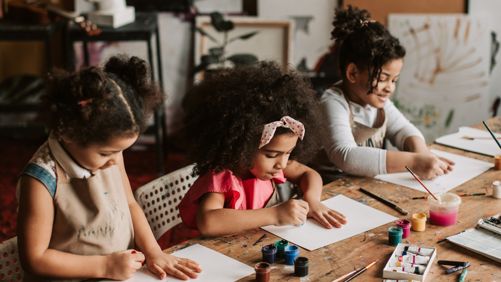 Three children sit at a table and draw on pieces of paper