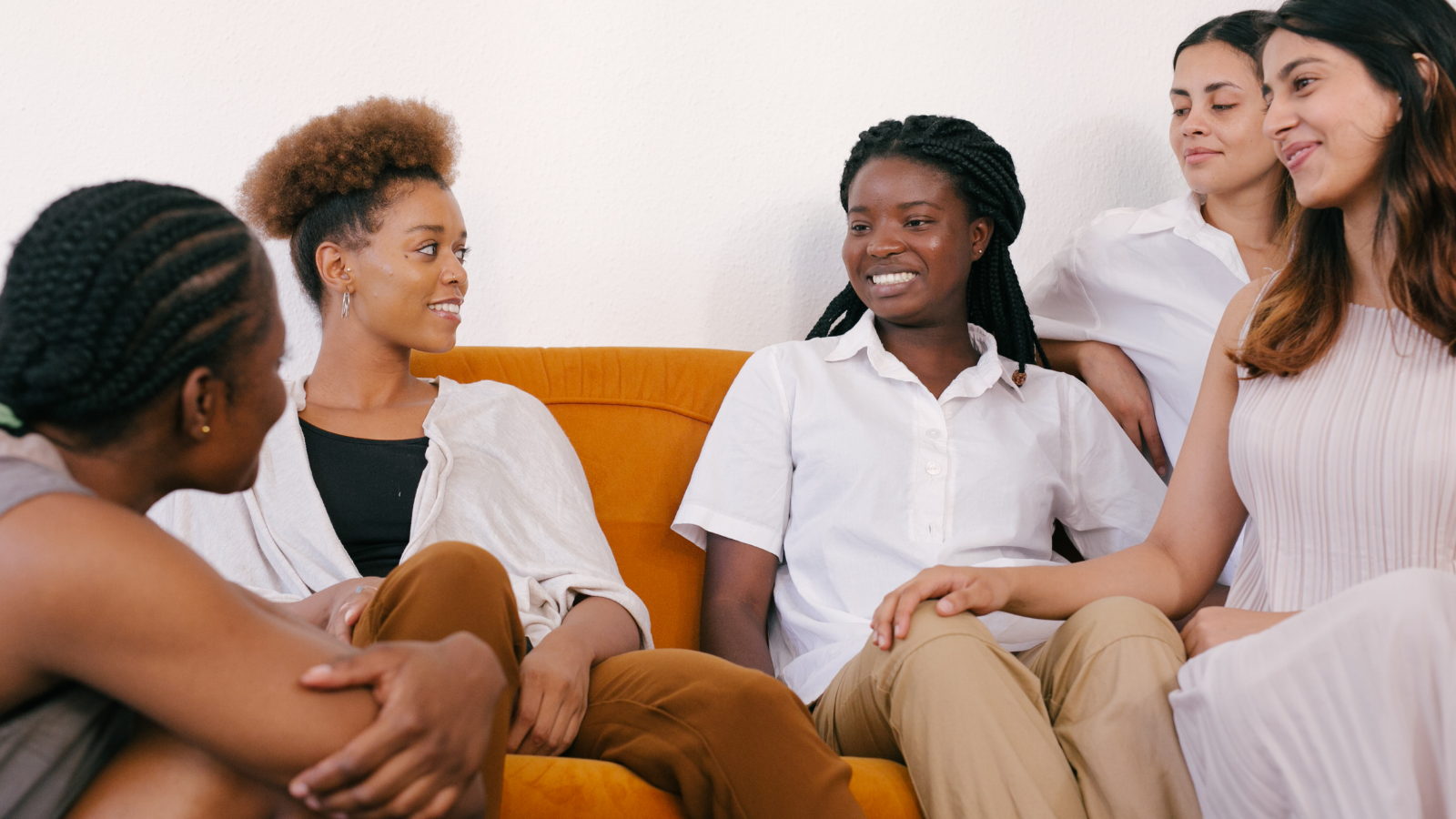 A group of young woman sit on a orange sofa and sit have a discussion