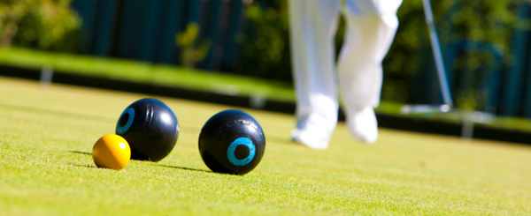 A bowling green showing a person hitting the biased bowls towards a jack