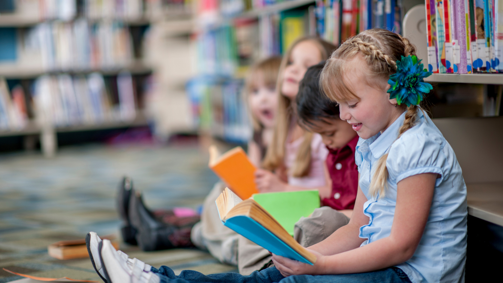 Three girls and a boy read books on the floor at the library