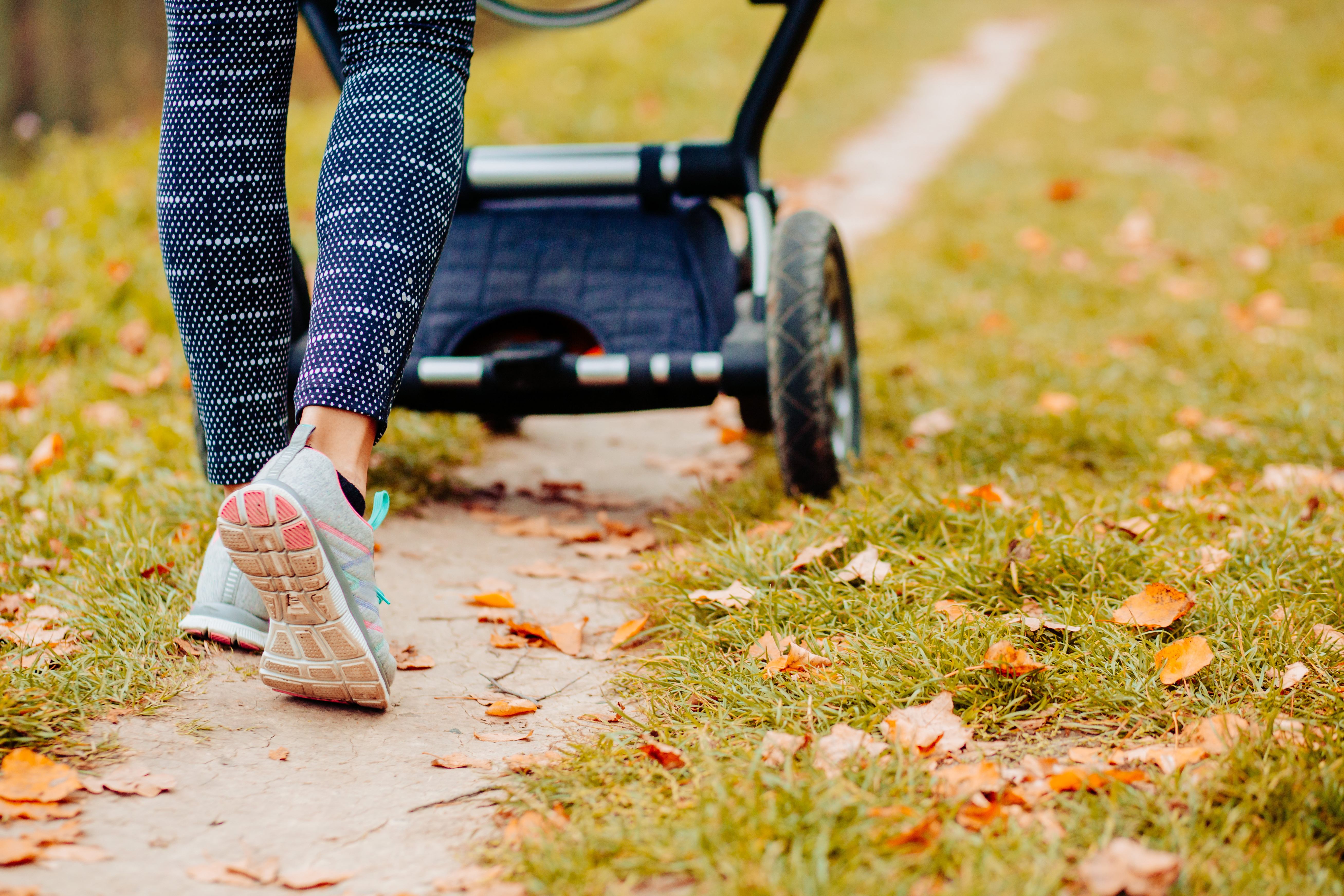 A closeup of a person's legs as the walk at the park with a pram