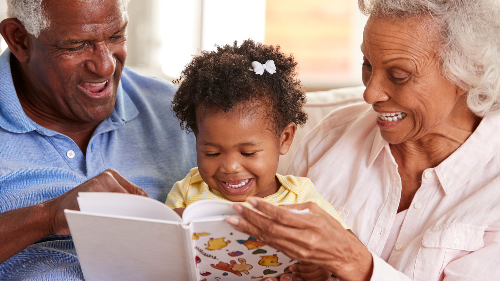 An older black man and woman read a book to their grandaughter