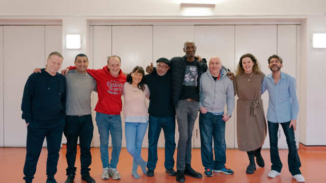 A groups of adults stand in a line and pose for a photo with their arms around each others shoulders