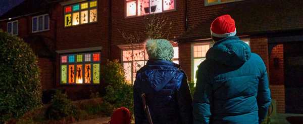 Two people admire houses with windows decorated with coloured paper and lights 